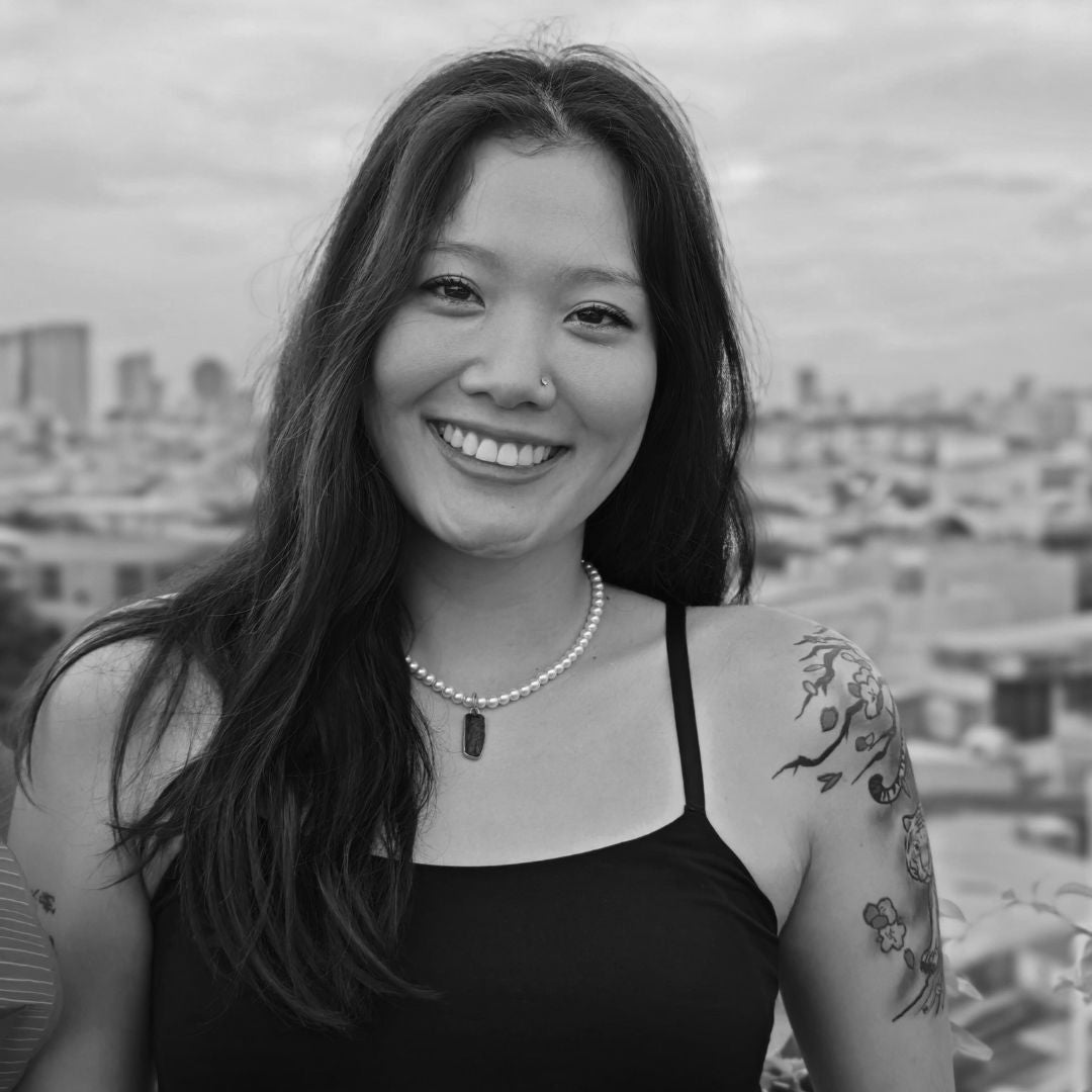 Black and white photo of a woman with tattoos smiling outdoors.